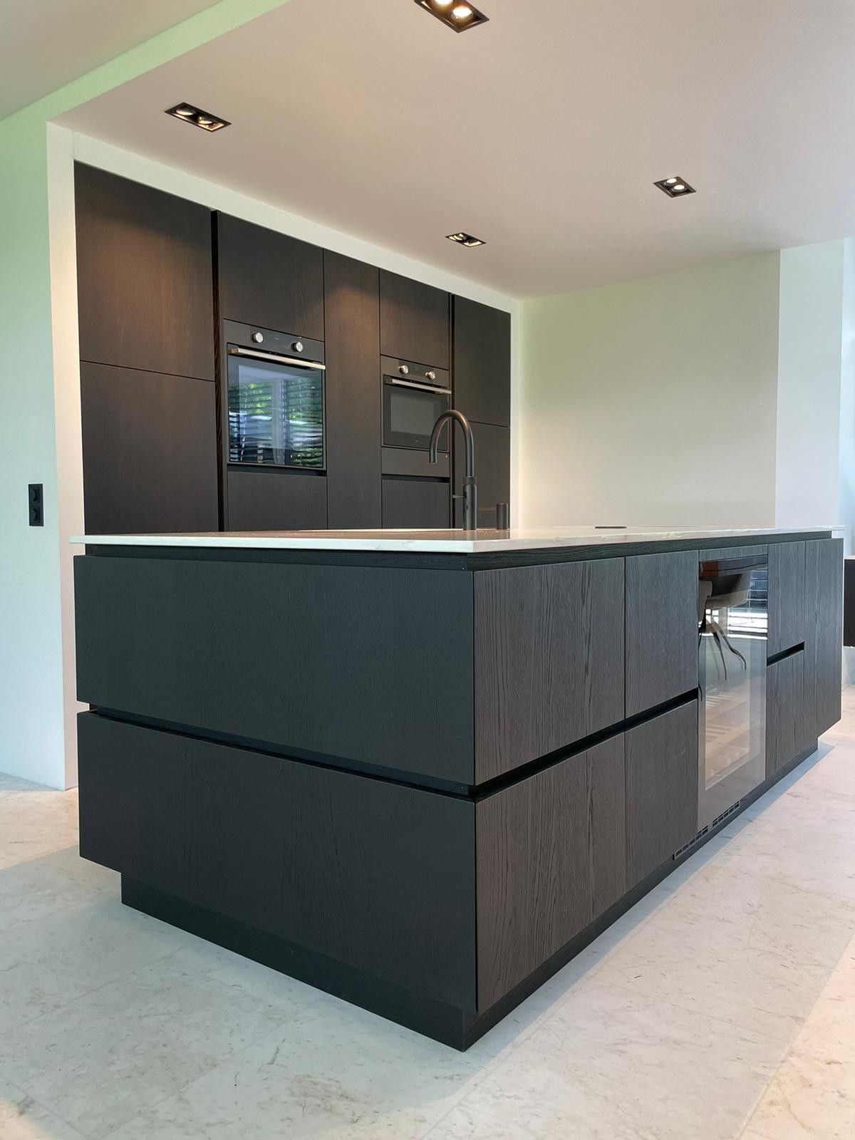 Zwart keukeneiland met kastenwand met licht blad